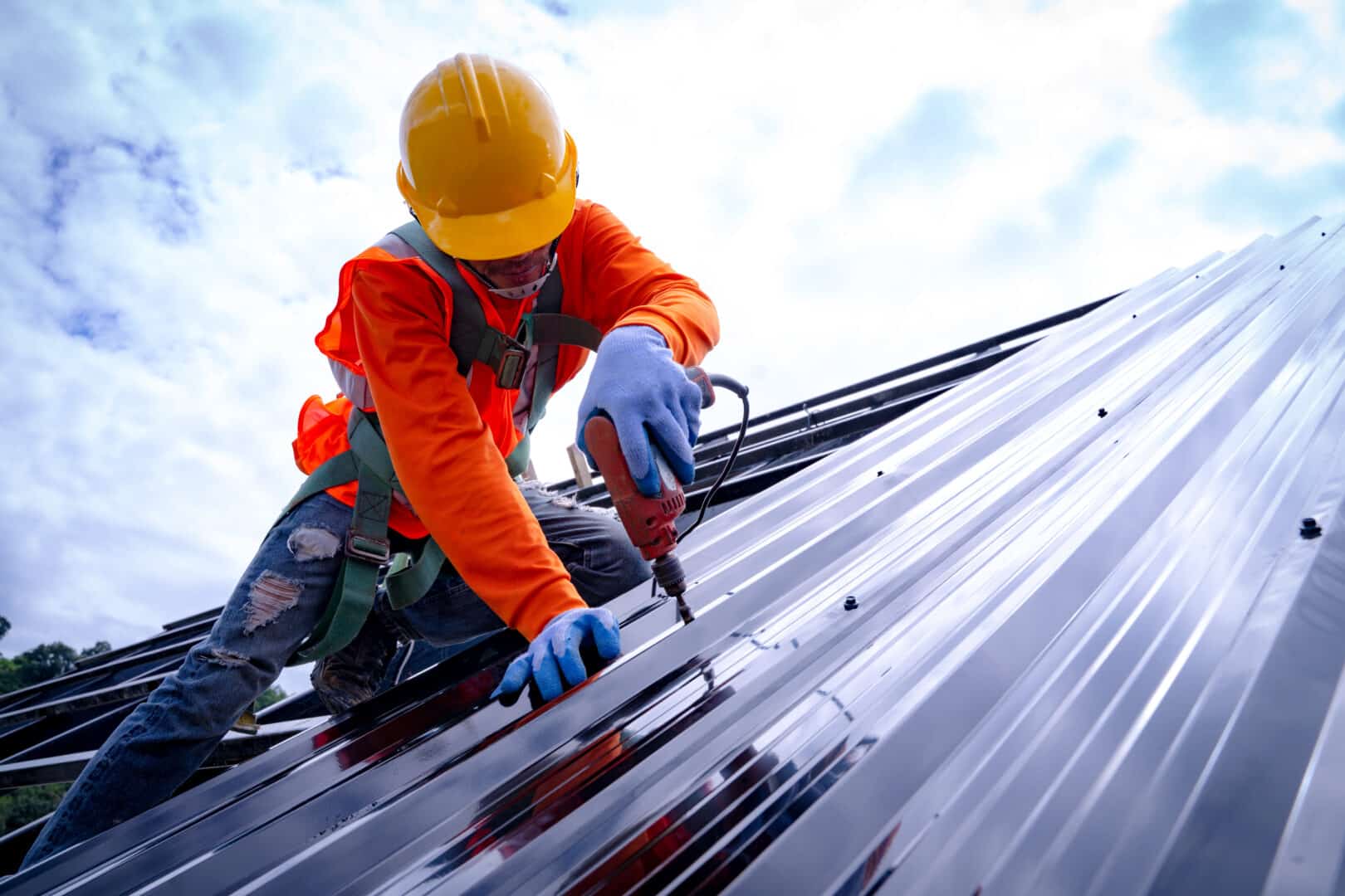 A man is on top of a steel roof installing it with a drill.